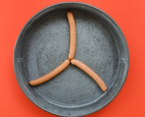 Drei Wiener angeordnet als Propeller in einer silbernen Schüssel platziert auf orangenem Hintergrund